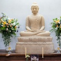 A lay guest decorates the sandstone Buddha with fresh flowers.