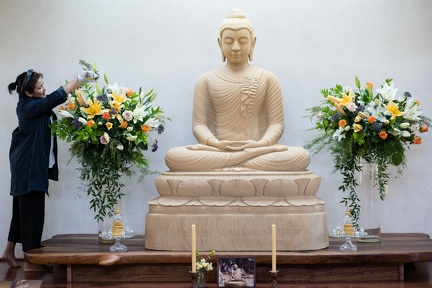 A lay guest decorates the sandstone Buddha with fresh flowers.