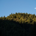 Morning sunlight crests a nearby mountain peak as the moon descends for the day.