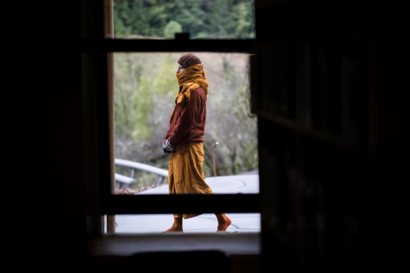 A sāmaṇera bundles up against the cold as he does walking meditaiton outside the library window.