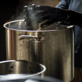 Dhammavaro wears heavy gloves to manipulate cloth soaking in the boiling reduction bath, which helps to saturate the garment with dye. Beginning with two 40-gallon barrels of madrone bark, the resulting dye would fill only a single, 10-gallon pot.